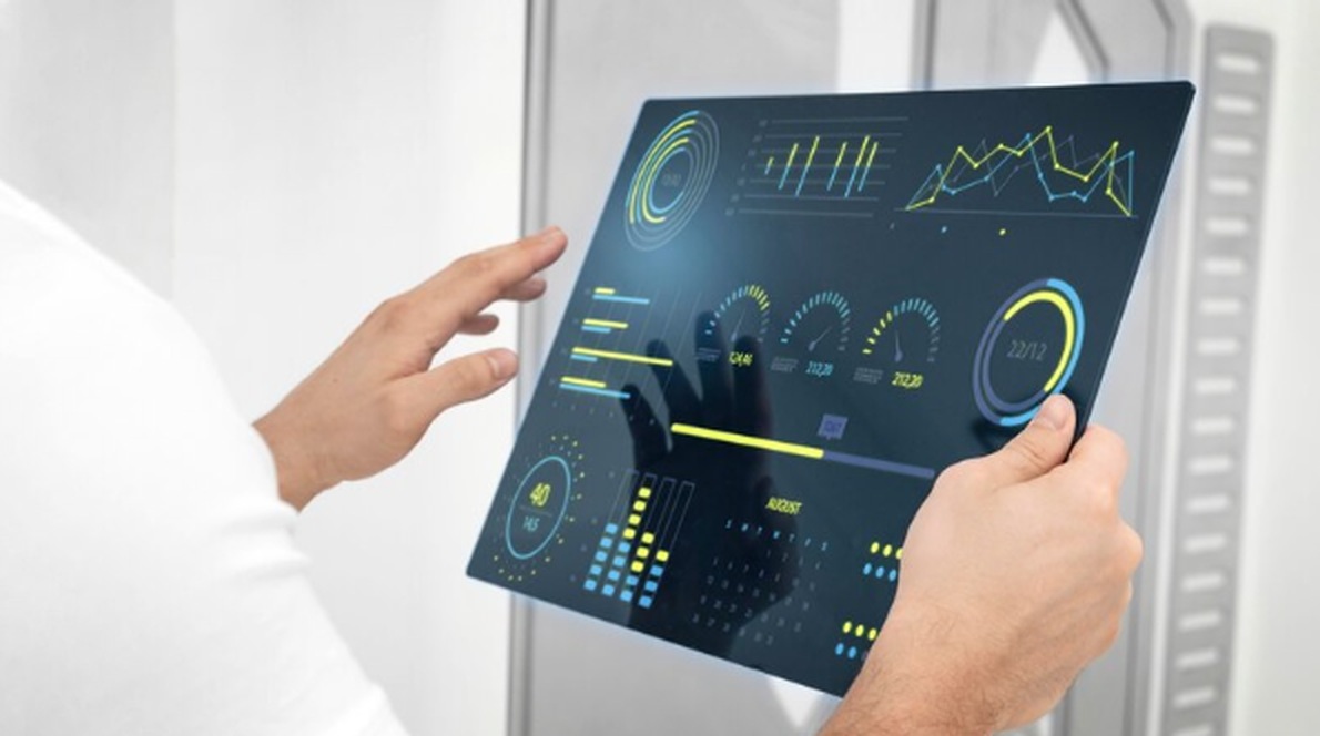A person holds a transparent digital tablet displaying futuristic financial dashboards with charts, metrics, and indicators, symbolizing data-driven strategies and the rise of automatic investments.