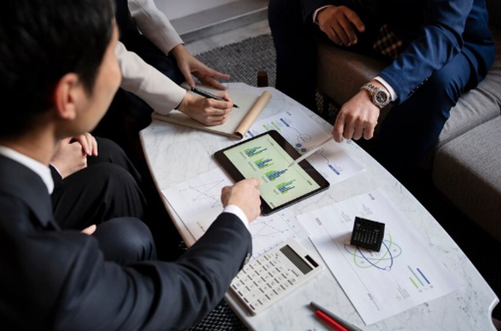 Business professionals reviewing financial charts on a tablet during a meeting, surrounded by printed reports, a calculator, and notepads—illustrating strategic planning for a diverse portfolio in Australia.