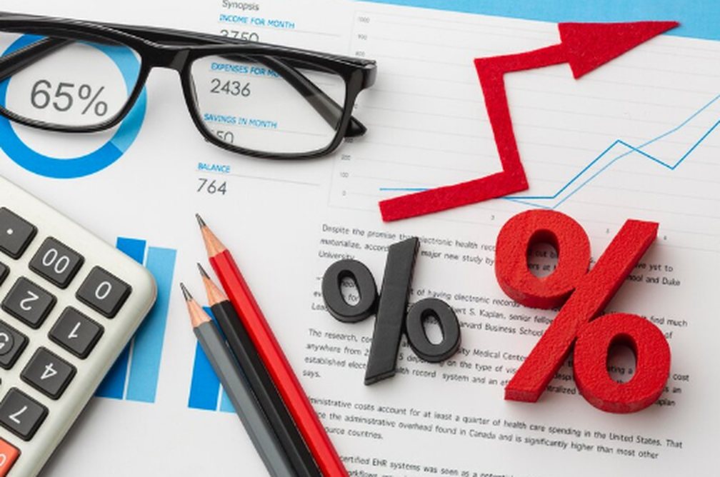 Desk with calculator, glasses, pencils, and financial documents displaying graphs and a large percentage symbol, representing analysis and fluctuations in interest rates.