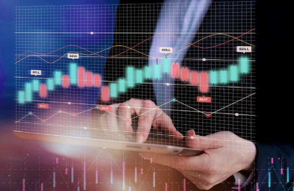 A person in a suit using a digital tablet with overlaid candlestick charts, buy/sell indicators, and trend lines, representing real-time data analysis and decision-making in financial investments.